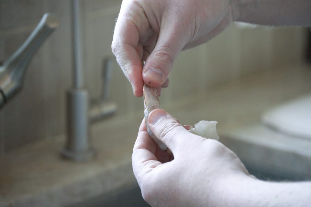 a hand begining to take of a shrimps tail shell