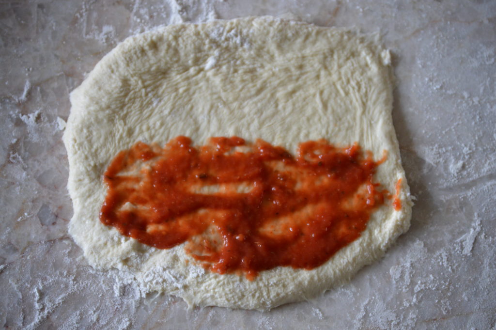 sauce being applied to the calzone dough