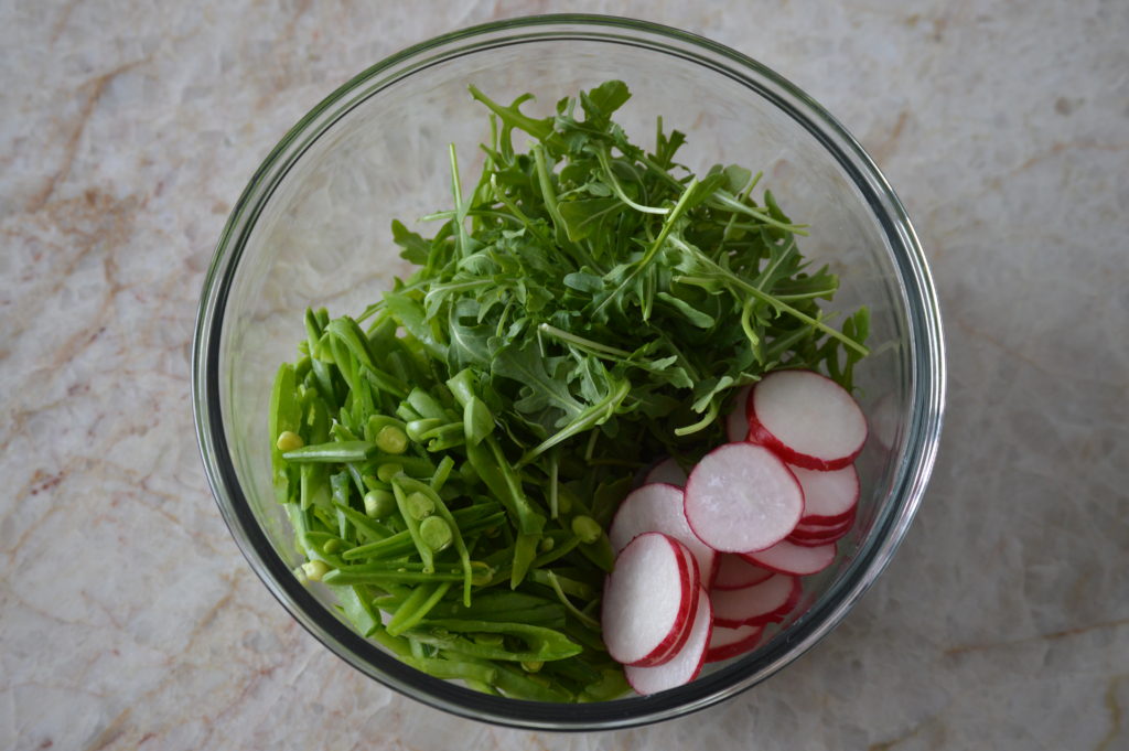 the sliced snap peas, radish, and arugula is in a mixing bowl