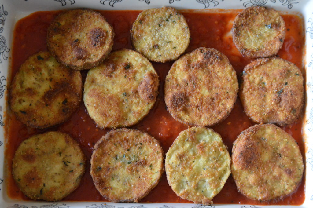 the fried eggplant is placed over sauce in the bottom of a casserole dish