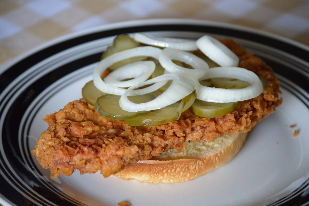 the pork tenderloin sandwhich topped with pickles and onion