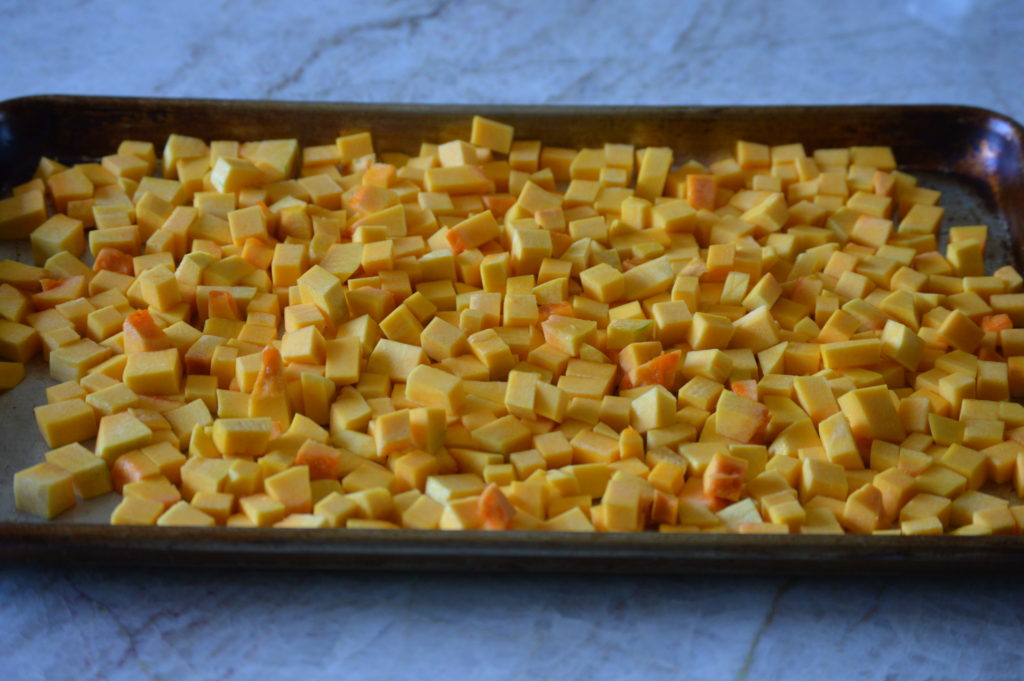 the cubbed butternut squash is on a baking sheet and ready for the oven