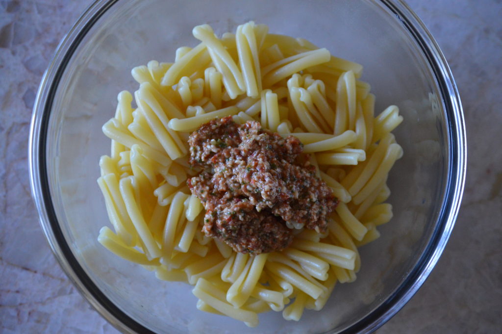 cooked pasta and some pesto alla trapanese in a mixing bowl