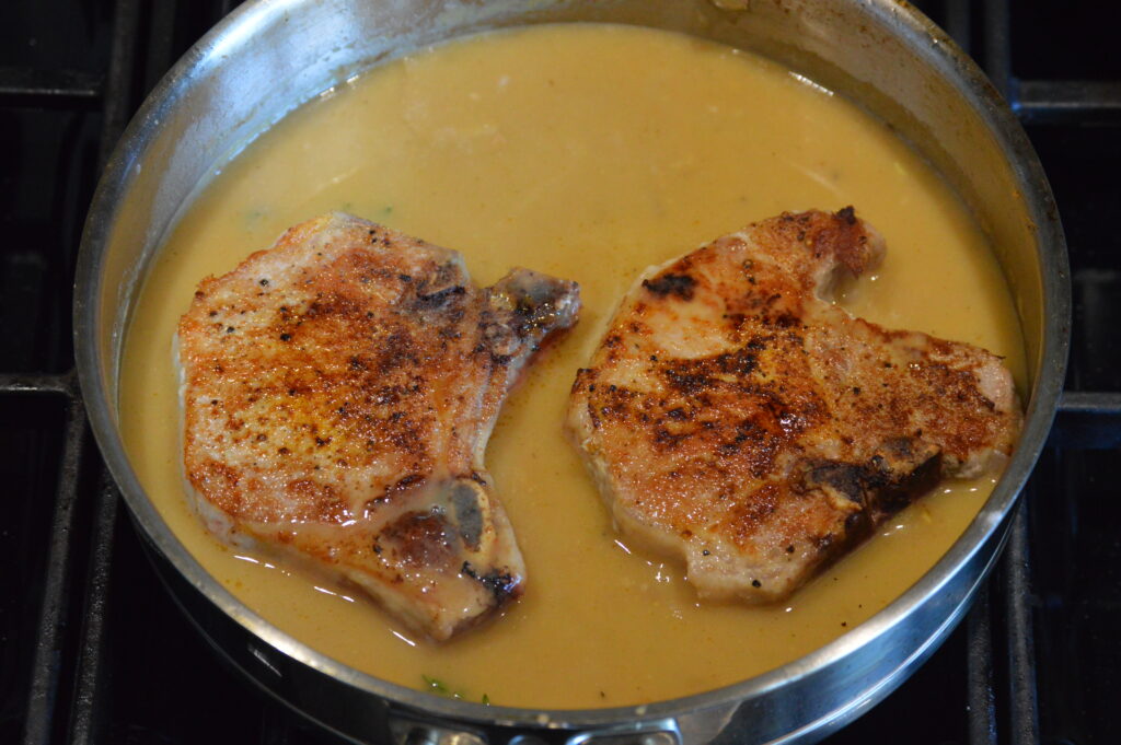 the pork chops are placed back in the pan with the smothering sauce to finish cooking